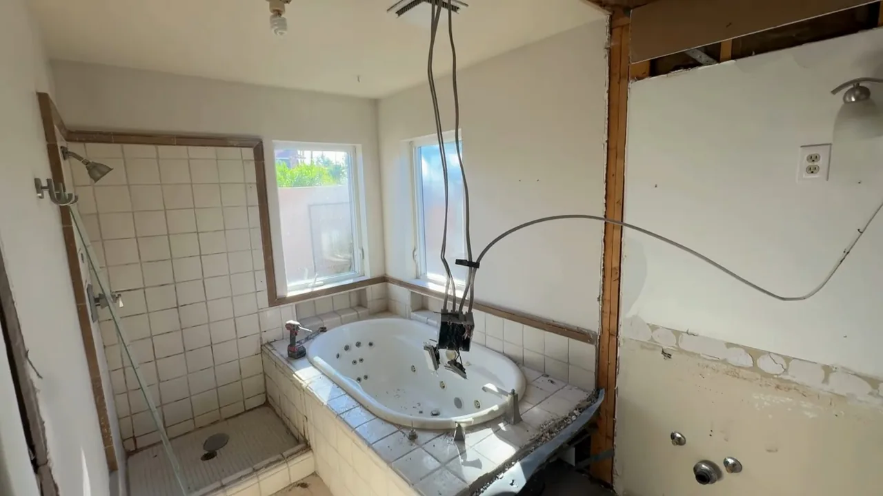 Bathroom with its walls opened to the studs around a tub and a tiled shower area.