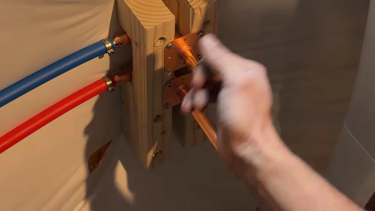 Hand holding a copper stub beside blue and red PEX lines clamped to a wooden block.