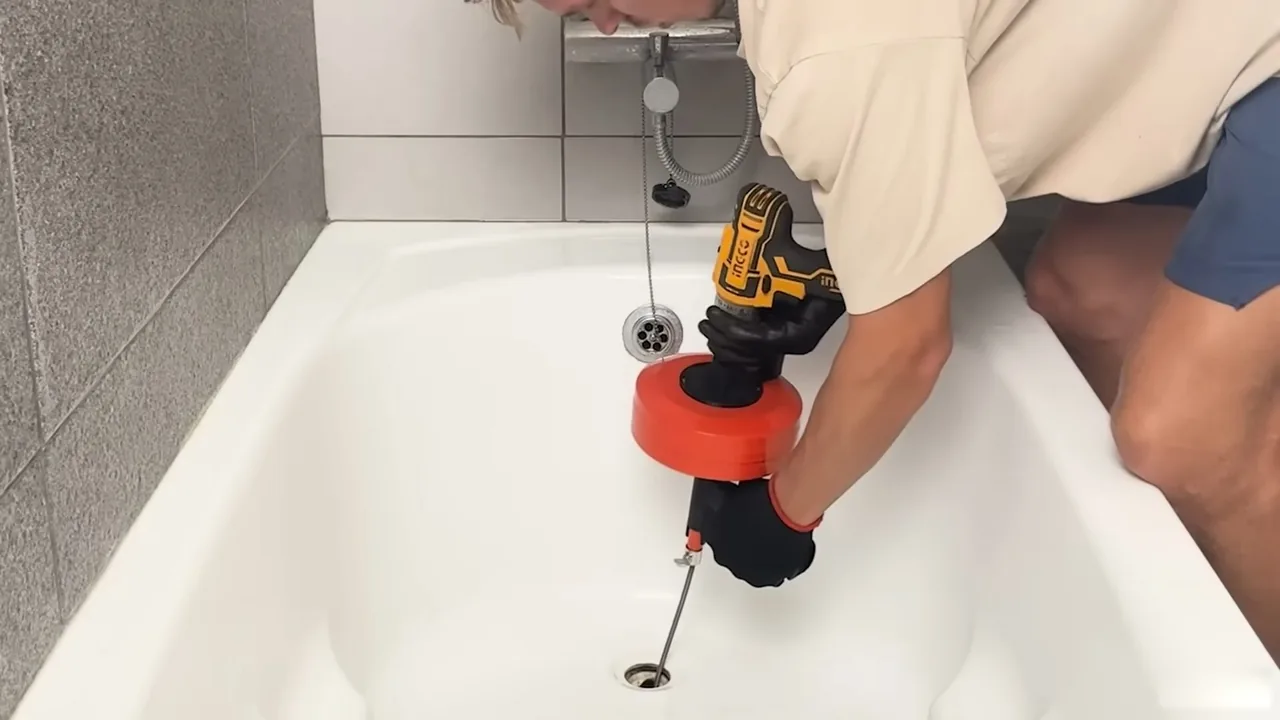 Person running a cable drain auger with a cordless drill down a bathtub drain.