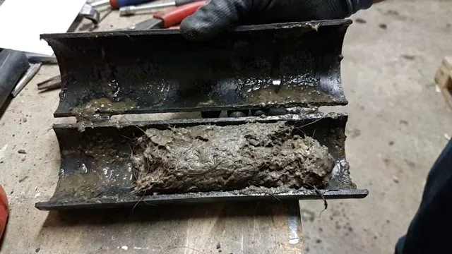 Drain pipe sawn open lengthwise to show a thick layer of packed debris along the inner wall.