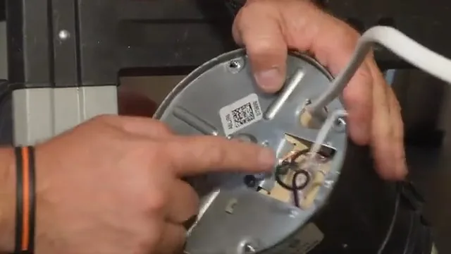 Hands holding the base plate of a garbage disposal while a finger points at its wiring connections.