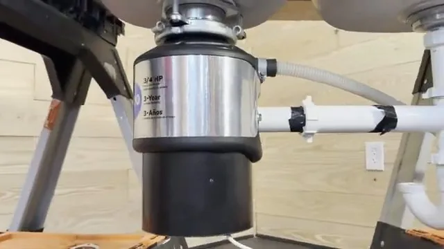 Garbage disposal hanging from a sink with a taped white discharge pipe and a grey hose attached.