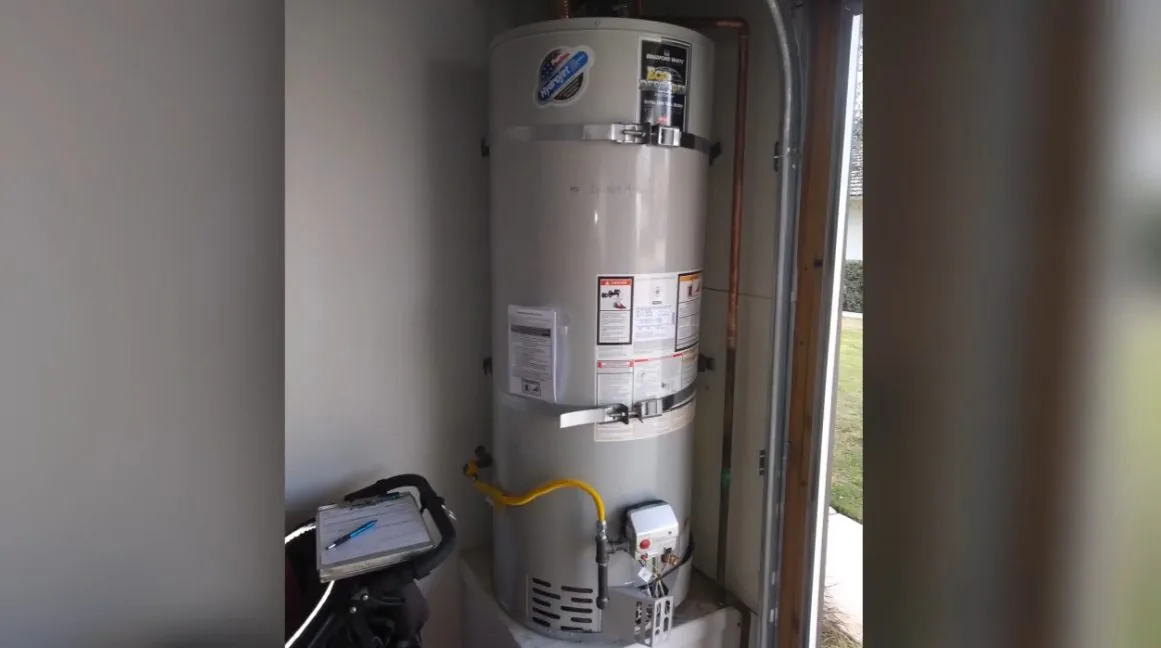 Gas water heater in a narrow closet with a yellow flexible gas line and a controller box at its base.