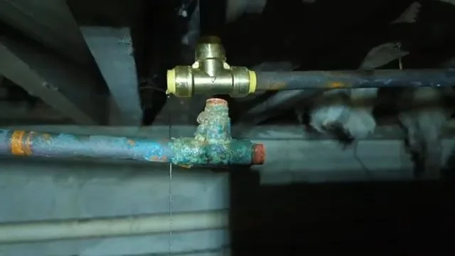 Corroded copper pipe with green deposits joined to a brass tee beneath floor framing.