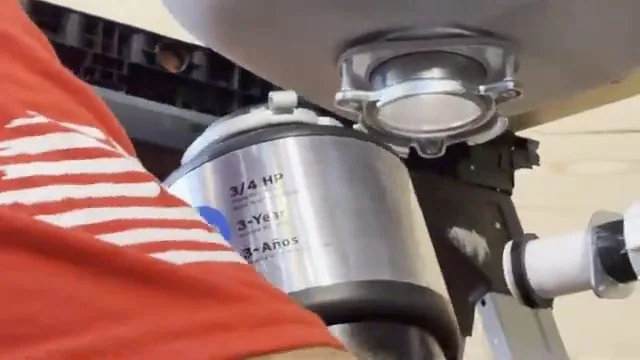 Person in a red striped shirt holding a garbage disposal mounted under a sink bowl.