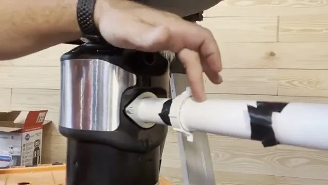 Hand resting on a garbage disposal with a taped white drain pipe connected at its side.