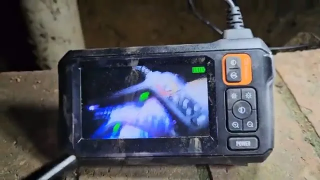 Handheld inspection monitor resting on the ground, its screen showing a view inside a pipe.