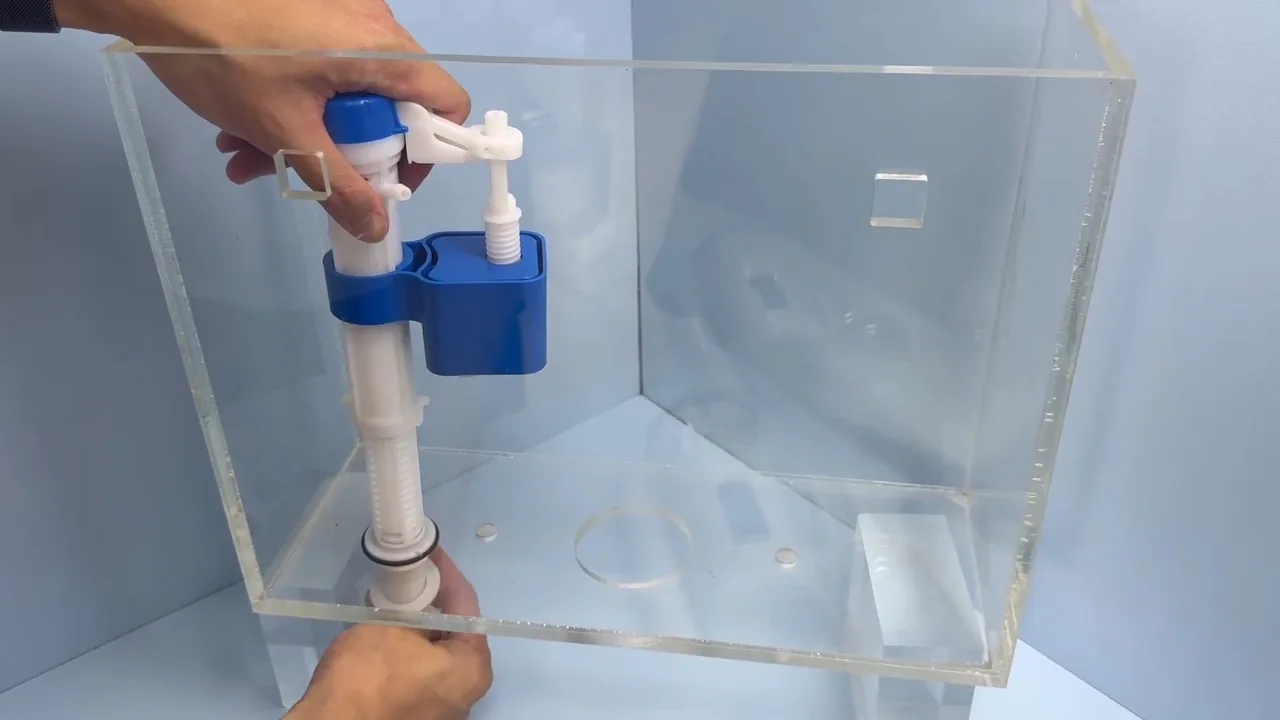 Hands adjusting a blue and white fill valve inside a clear demonstration toilet tank.