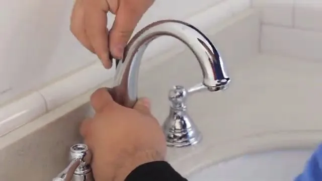 Hands holding the curved spout of a chrome faucet at a bathroom basin.