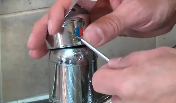 Hands removing a small screw from the handle of a chrome mixer faucet.