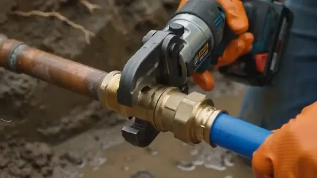 Orange-gloved hands holding a battery press tool on a brass valve that joins copper to blue PEX tubing.
