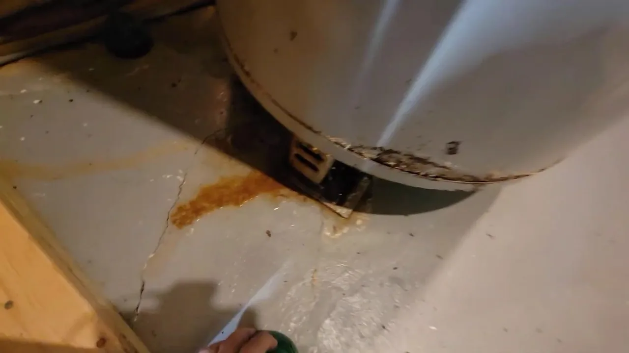 Rust-coloured staining and moisture on the floor around the base of a water heater tank.