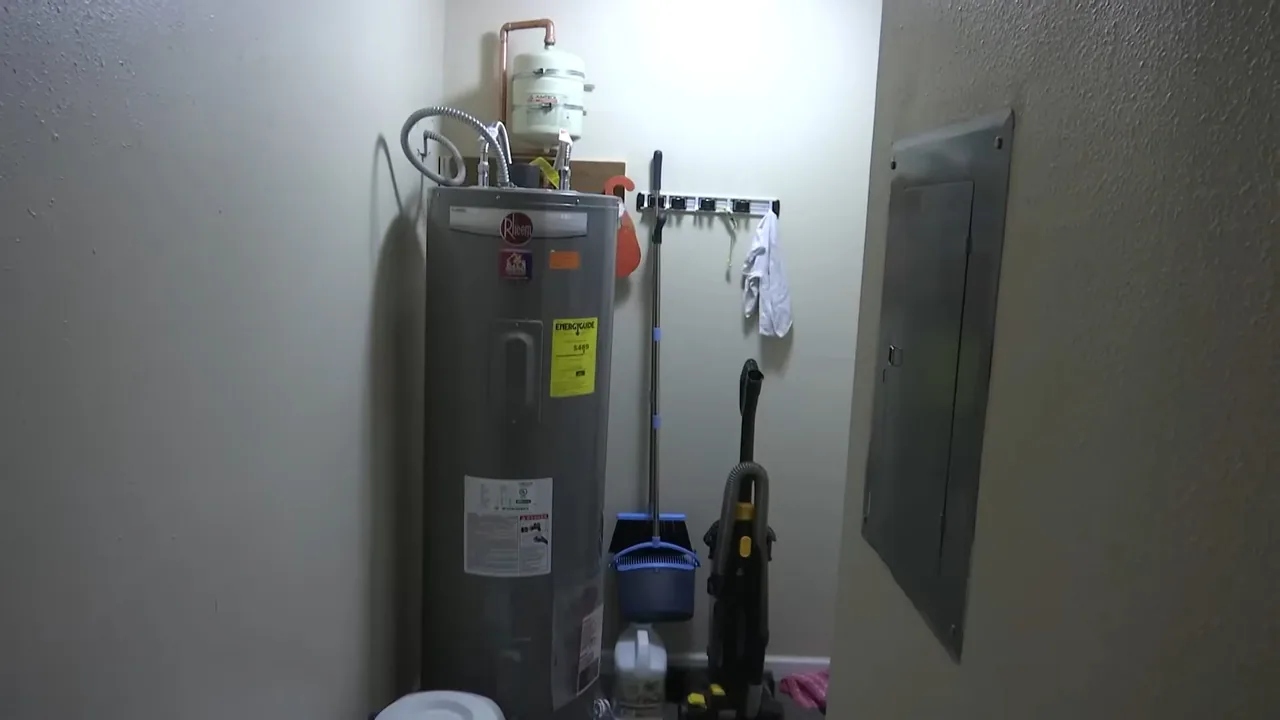 Tall tank water heater standing in a utility room beside an electrical panel.