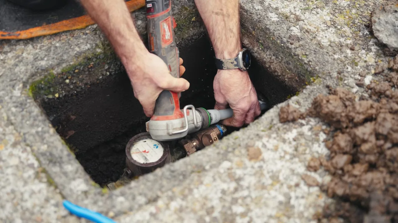 Technician using a power tool on a valve beside a water meter in an in-ground box.