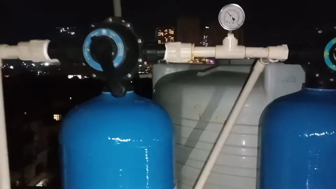 Two blue pressure tanks joined by white pipe with a round gauge on top, photographed against a night skyline.