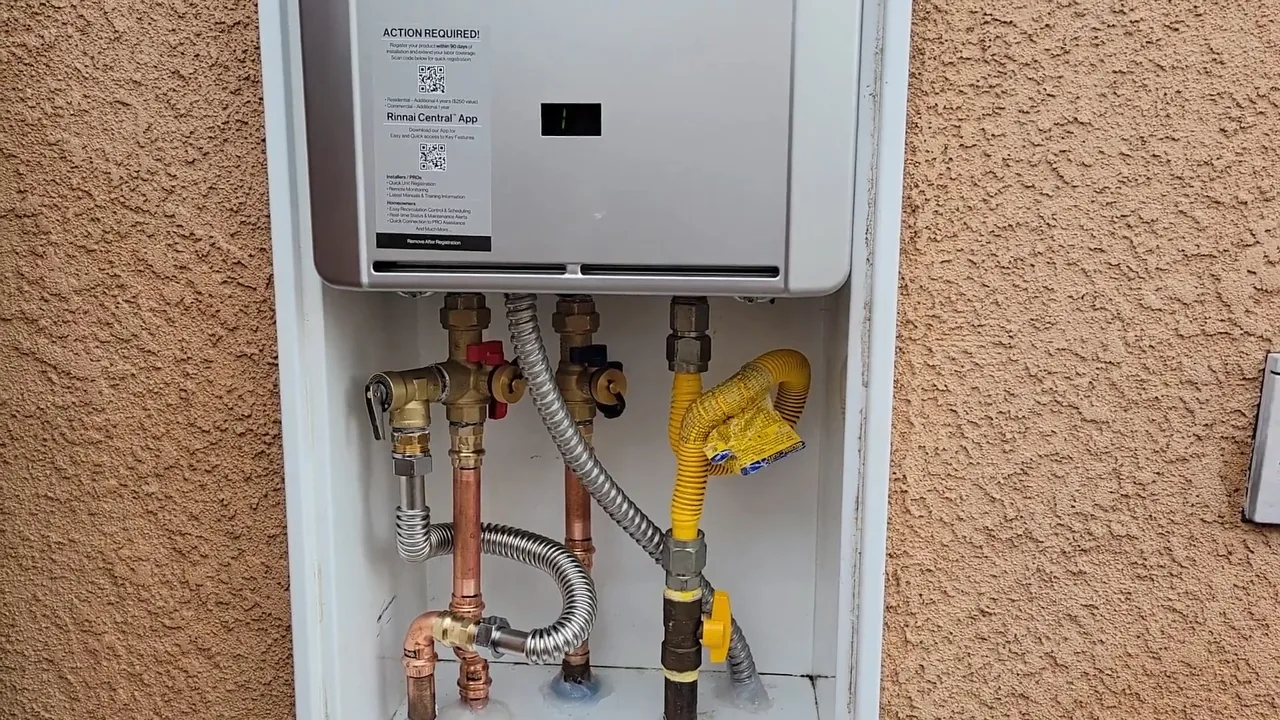 Wall-mounted tankless water heater inside a recessed cabinet in a stucco wall, with gas and water connections below it.