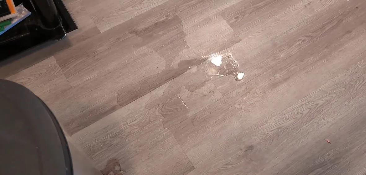 Water droplets and a damp patch on grey wood-look plank flooring.