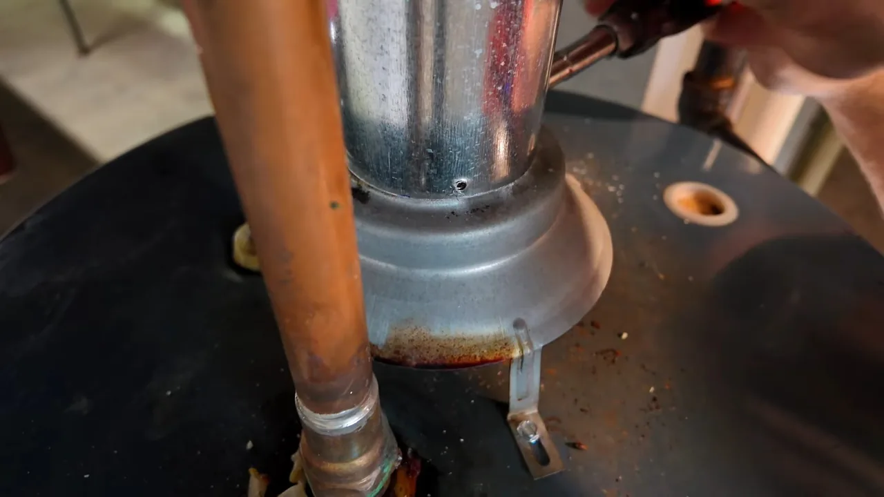 Top of a water heater tank with a metal flue collar and a copper pipe rising beside it.