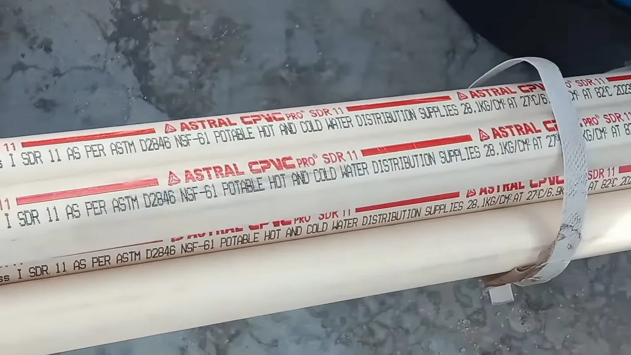 White plastic pipe lying on a dark floor with red printed text along its length naming the material and rating.