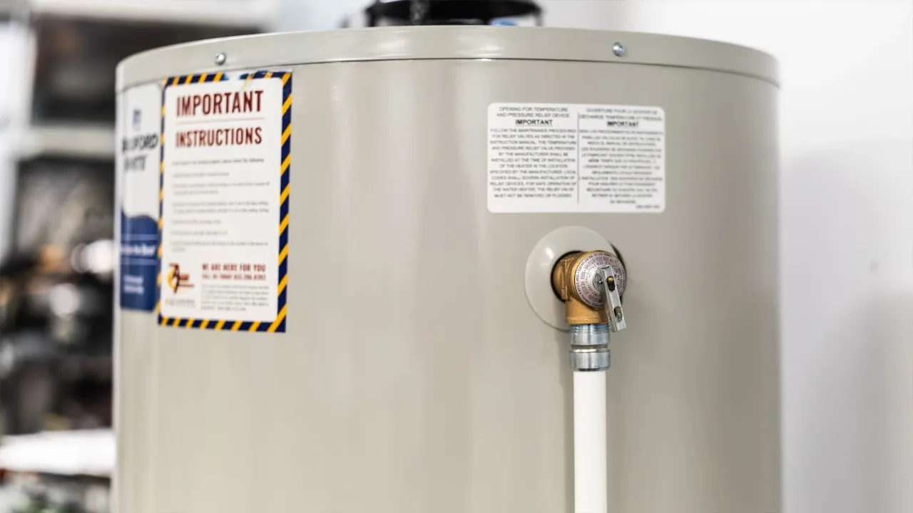White water heater tank with a printed instruction label and a brass fitting with a white line attached.